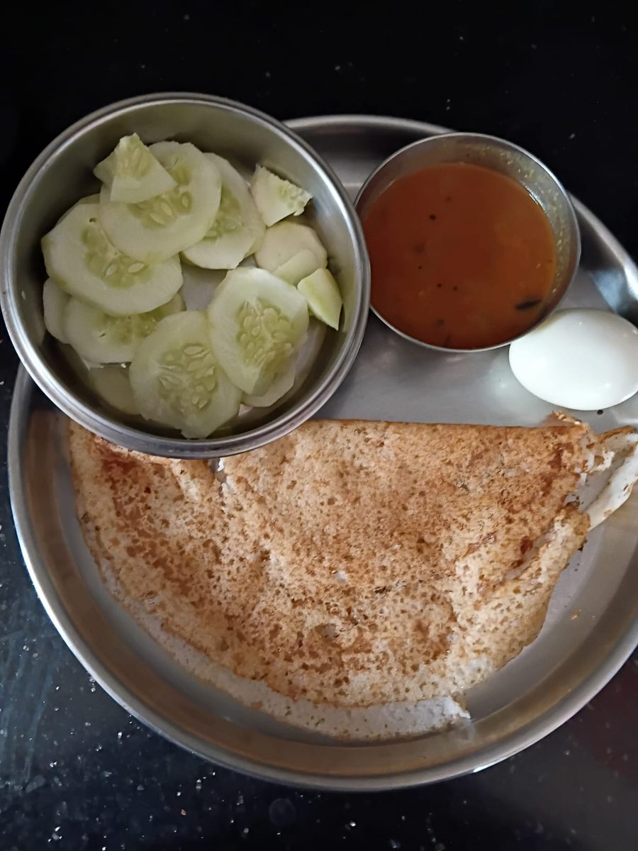 A breakfast plate: dosa with a boiled egg, sambar, and sliced cucumber