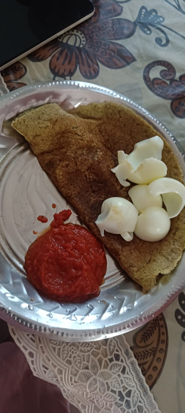 A ragi dosa with boiled egg whites and tomato chutney on a steel plate