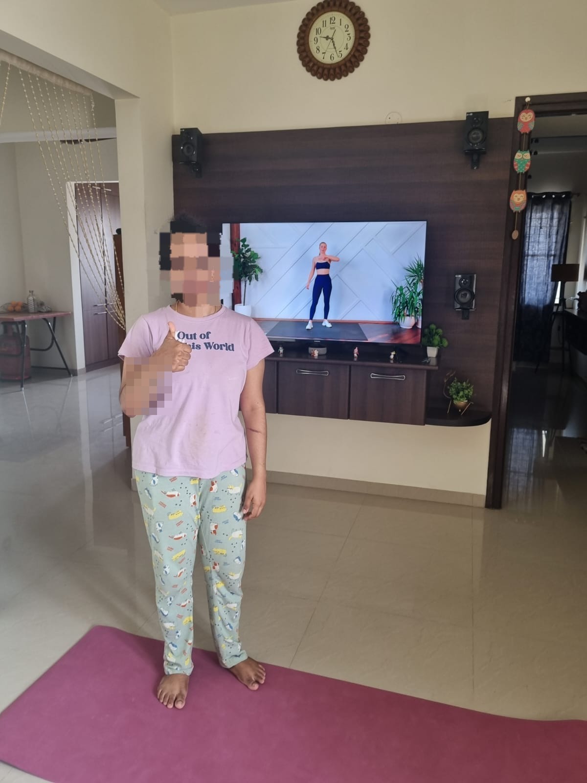 Nithya following a guided home workout on her yoga mat, giving a thumbs up