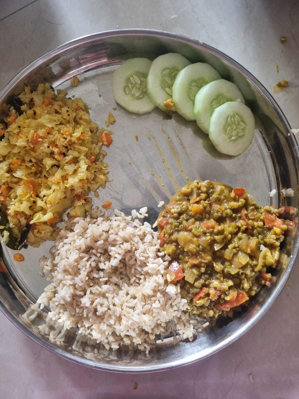 A balanced plate of brown rice, whole green moong dal, a cabbage and carrot poriyal, and cucumber slices